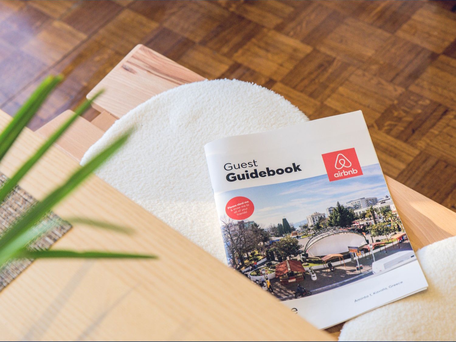 No fundo, há uma mesa de madeira clara com uma revista chamada 'Guest Guidebook', que exibe imagens de um destino turístico. Ao lado, aparecem detalhes de uma planta e uma cadeira acolchoada, reforçando um ambiente aconchegante e convidativo. A composição sugere dicas práticas e planejamento para melhorar a experiência de hóspedes.