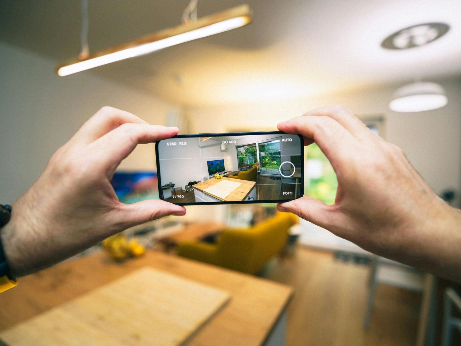 Uma pessoa fotografa o interior de um imóvel com um smartphone, capturando detalhes da decoração e iluminação natural. A cena ilustra a importância de boas imagens na divulgação de propriedades.