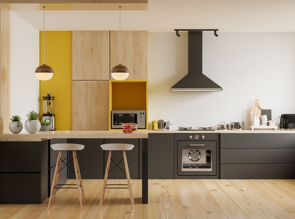 Cozinha moderna e aconchegante, com design minimalista. Os móveis combinam tons de amarelo e preto com madeira clara, criando um ambiente acolhedor e funcional. A bancada tem duas banquetas, iluminação pendente e itens decorativos que reforçam a sensação de conforto.